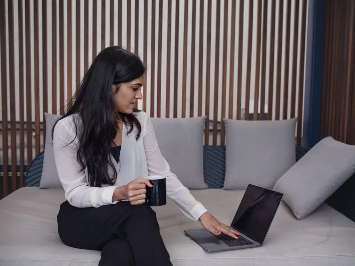 A woman on a sofa with a mug of coffee, calmly checking her laptop