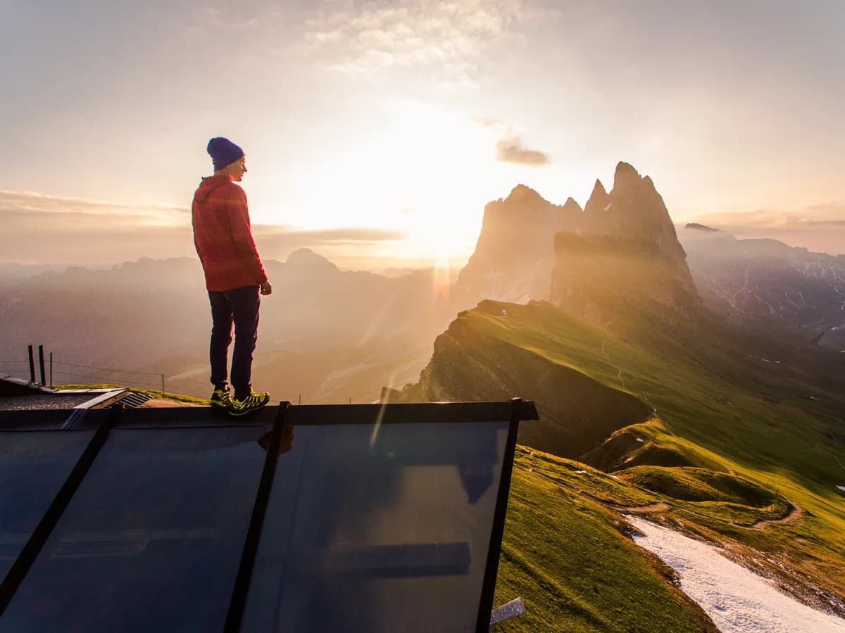 A hiker in a red jacket watching the sun rise over mountain peaks